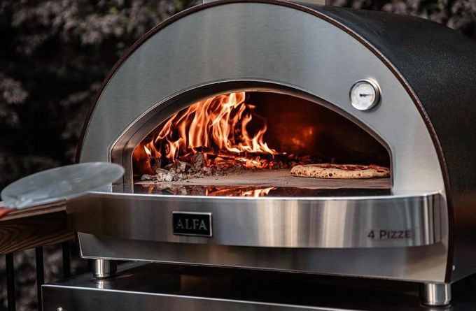 A pizza is being taken out of an outdoor pizza oven.