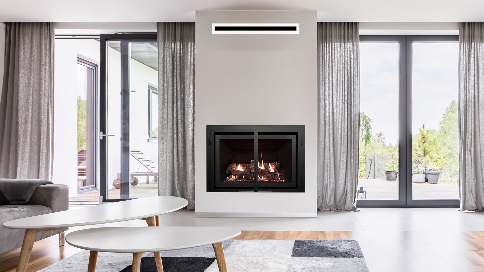 Living room with a fireplace, glass doors, and neutral décor. A fire burns inside the fireplace.