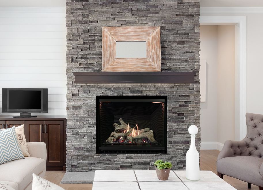 A living room with a stone fireplace, mantle with mirror, and a lit fire. There is a TV to the left and seating.
