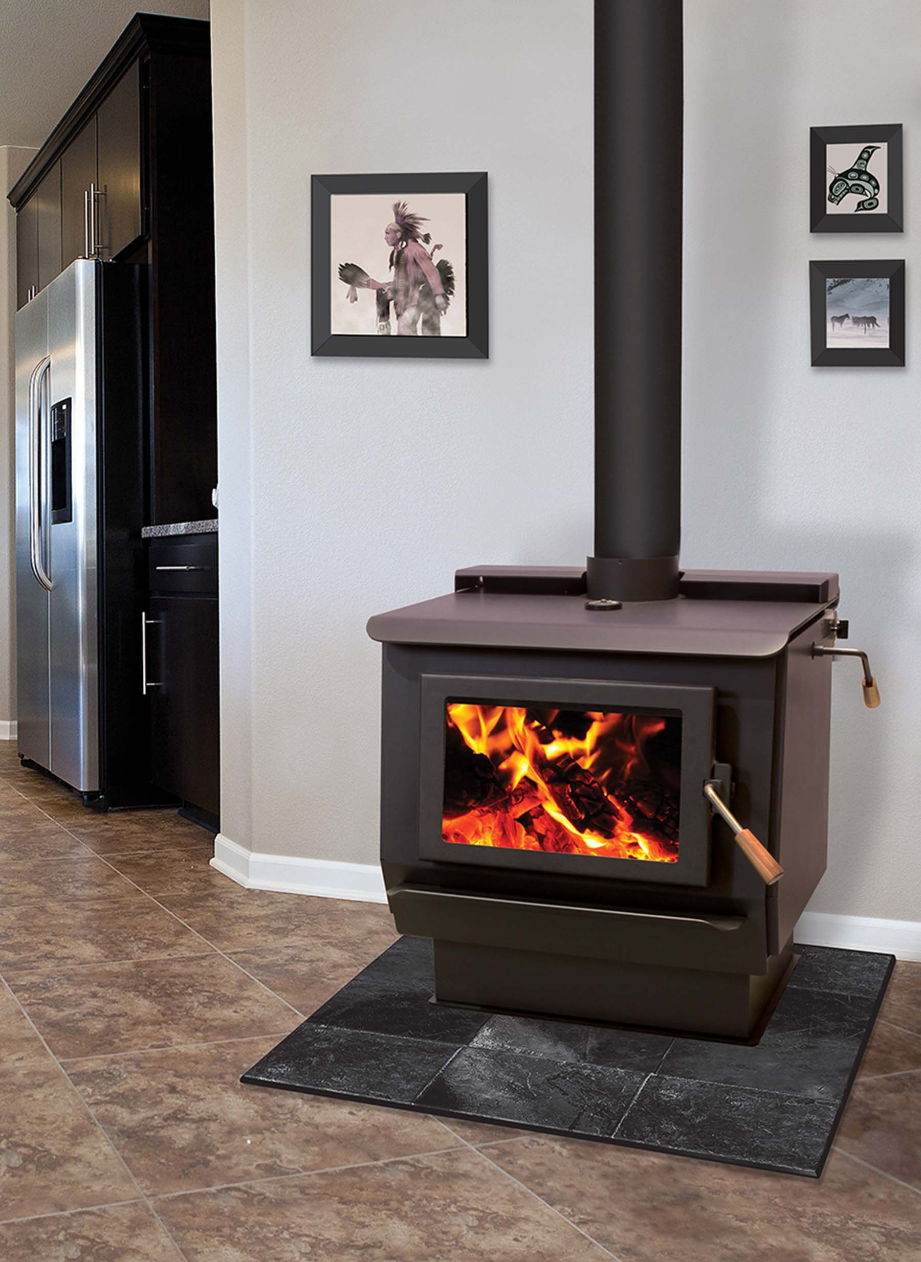 Wood-burning stove with fire inside, in a room with a refrigerator and pictures on the wall.