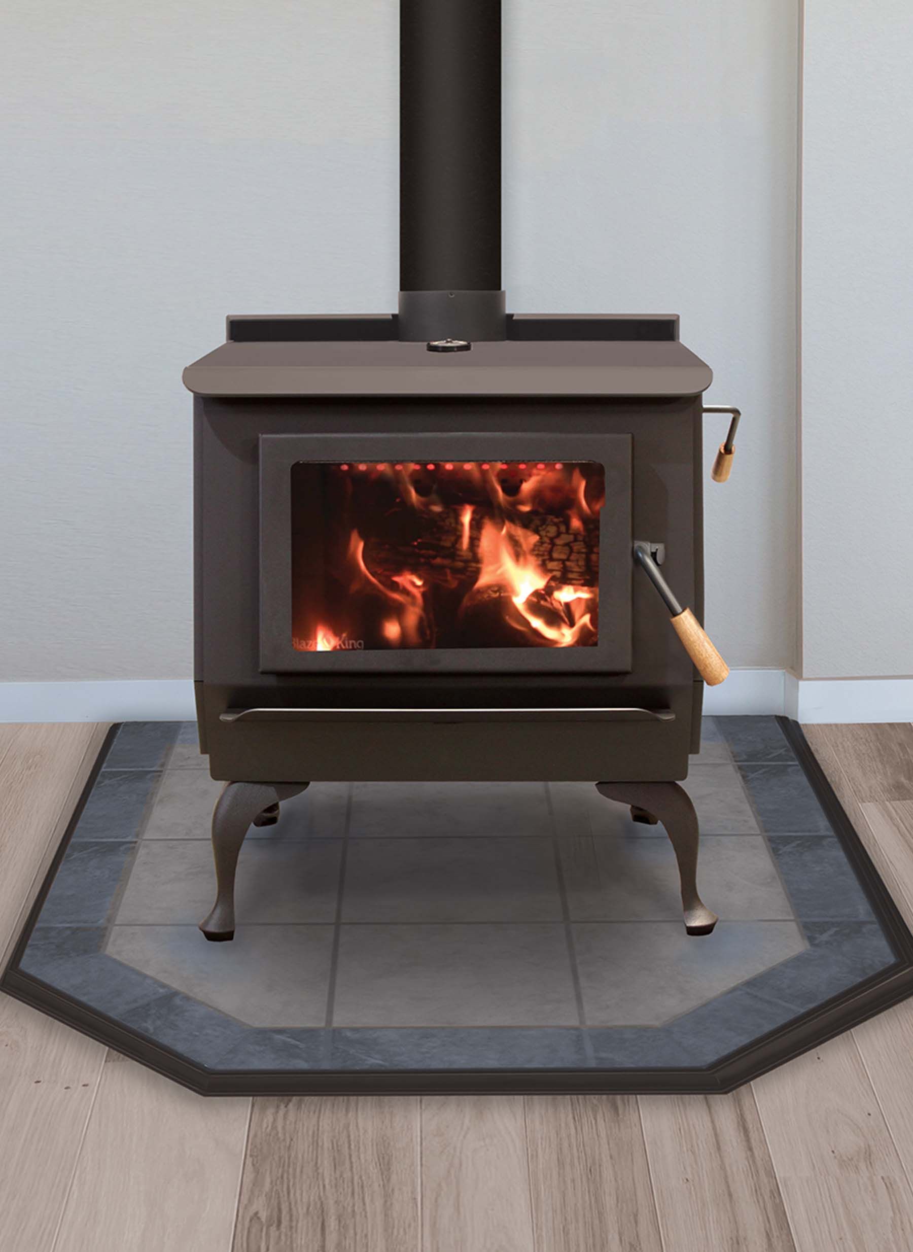 A wood-burning stove with flames inside, set on a tiled hearth, against a white wall.