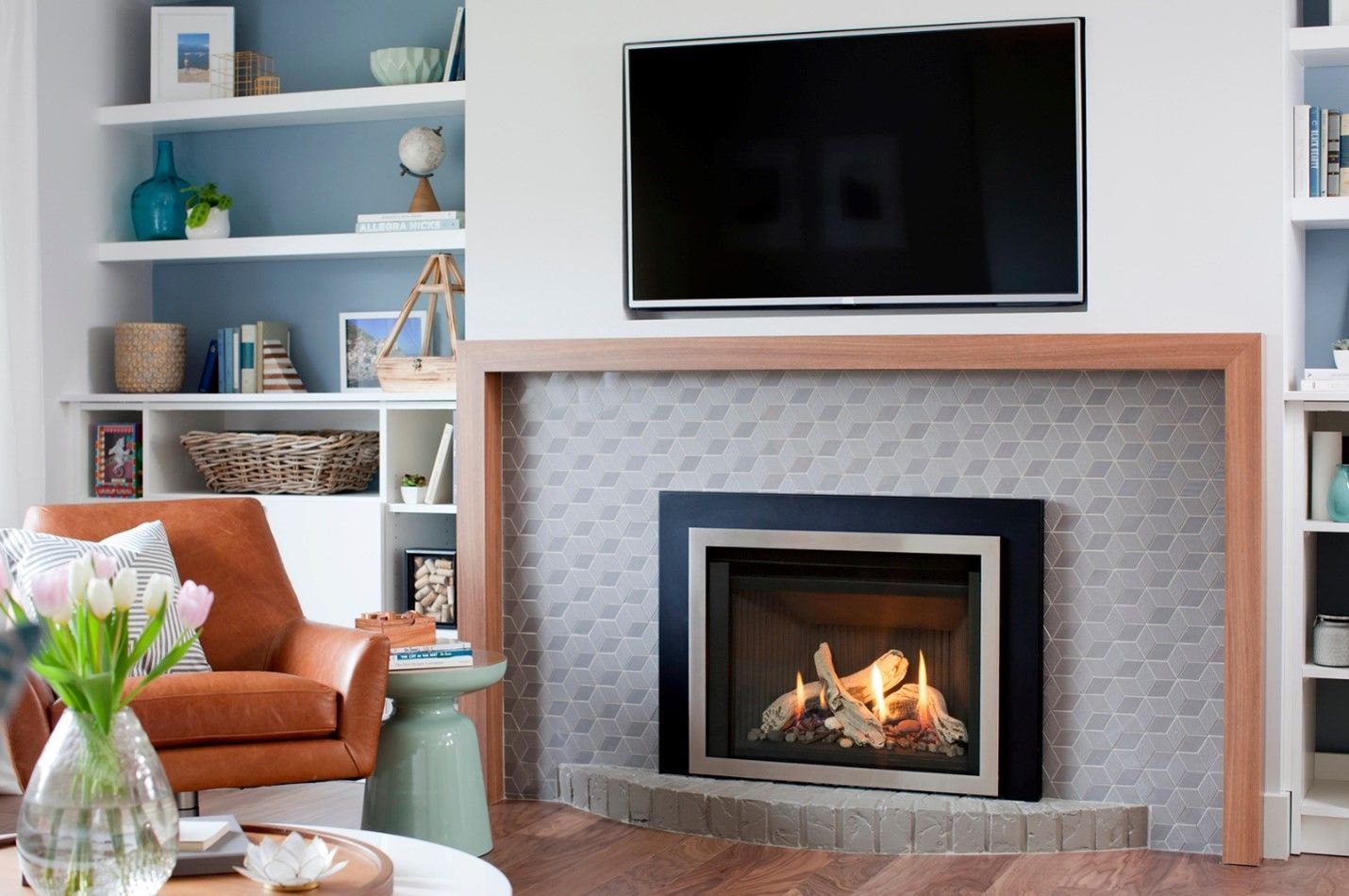 Living room with fireplace and mounted TV; built-in shelves on either side; a leather armchair sits nearby.