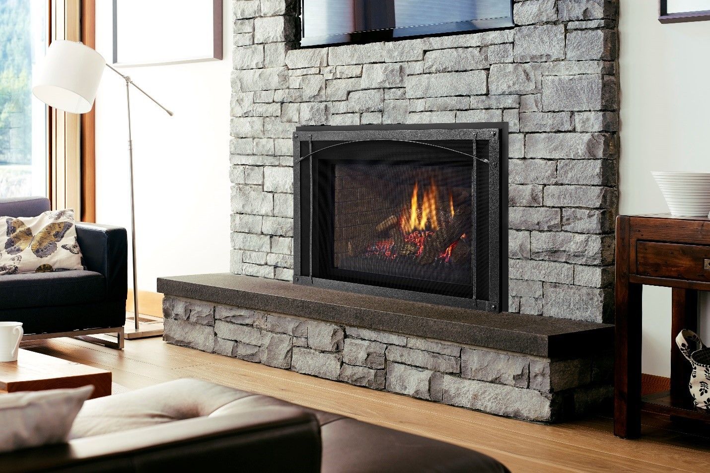 Stone fireplace with a lit fire, a black surround, and a stone hearth. A television is mounted above.