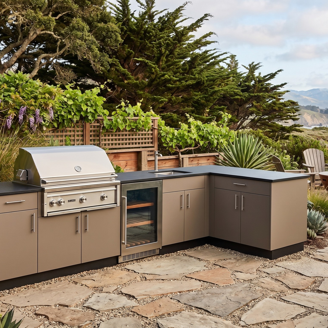 Outdoor grilling kitchen on a sunny patio with a gray cabinet, a grill, a Big Green Egg, and a sink. Palm trees and water in the background.