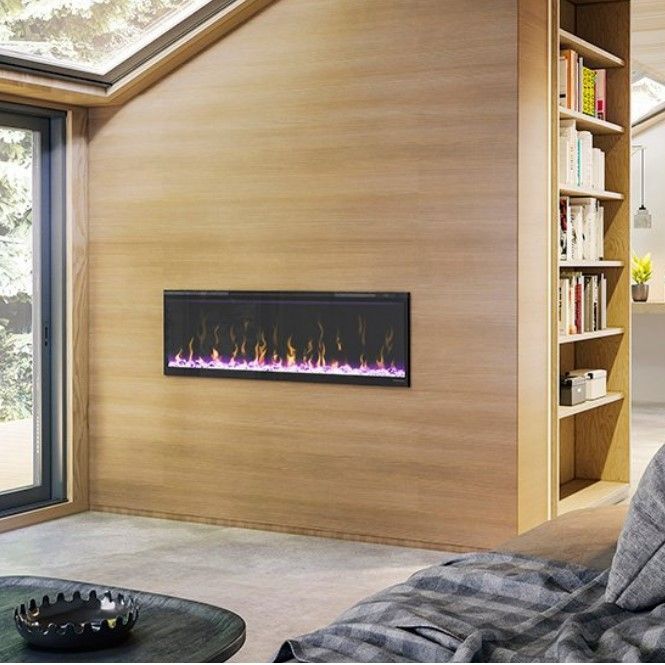 Electric fireplace mounted on a wood-paneled wall in a modern living room with a bookshelf. The fire's flames glow purple and orange.