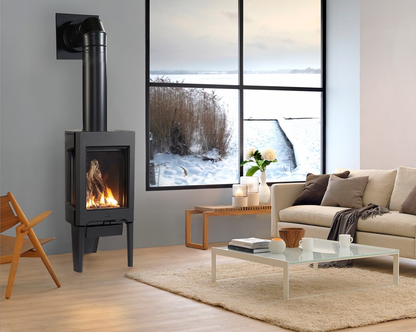 A modern living room with a fireplace, couch, and snowy view outside a large window. The fireplace has a lit flame.
