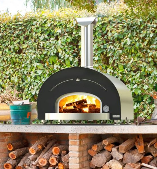 A red outdoor pizza oven with a pizza cooking inside, sitting on a wooden surface.