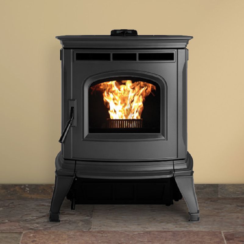 Black pellet stove with flames visible through the front window, set against a light brown wall and stone floor.