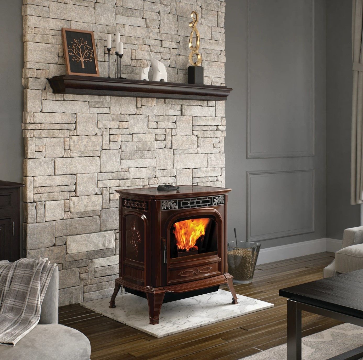 A dark brown, ornate wood stove with a fire burning, set against a stone wall, shelf with decorations, and gray walls.