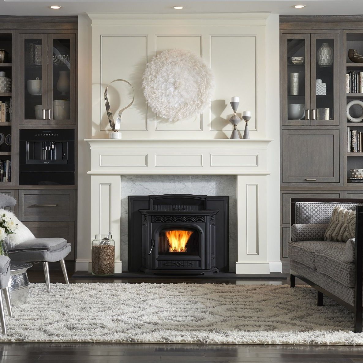 Living room with fireplace; a lit pellet stove is framed by white paneling, flanked by gray cabinets with display shelves.
