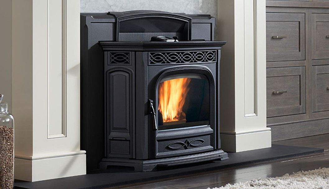 Black pellet stove with flames burning inside, set against a white fireplace surround. The backdrop is a kitchen with gray cabinets.