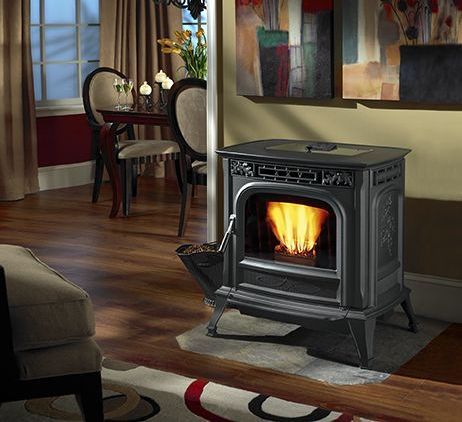 A black pellet stove with a lit fire in a cozy living room with hardwood floors and a dining area.