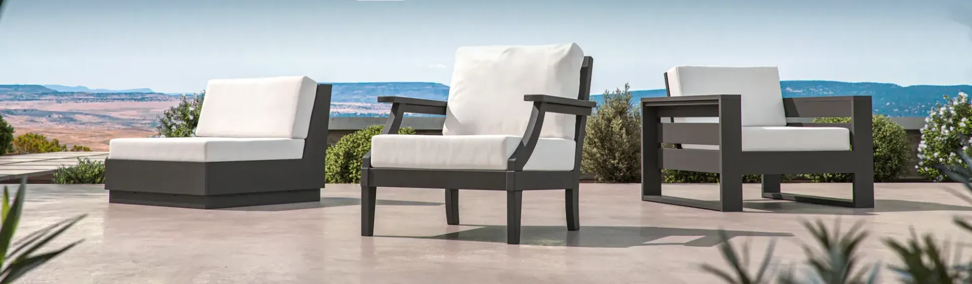 Three outdoor armchairs with white cushions sit on a patio overlooking a desert landscape and body of water.