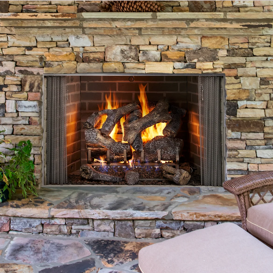 A modern fireplace with a lit fire is surrounded by a gray stone wall and topped by abstract art. Fireplace tools stand to the left.