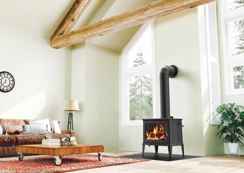 A cozy living room with a lit wood-burning stove against a light green wall, near a large window. Brown sofa, wooden beams, and decor.