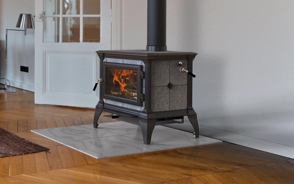 Wood-burning stove with lit fire in a room with white walls and a wooden floor. Stove sits on a light-colored tile.