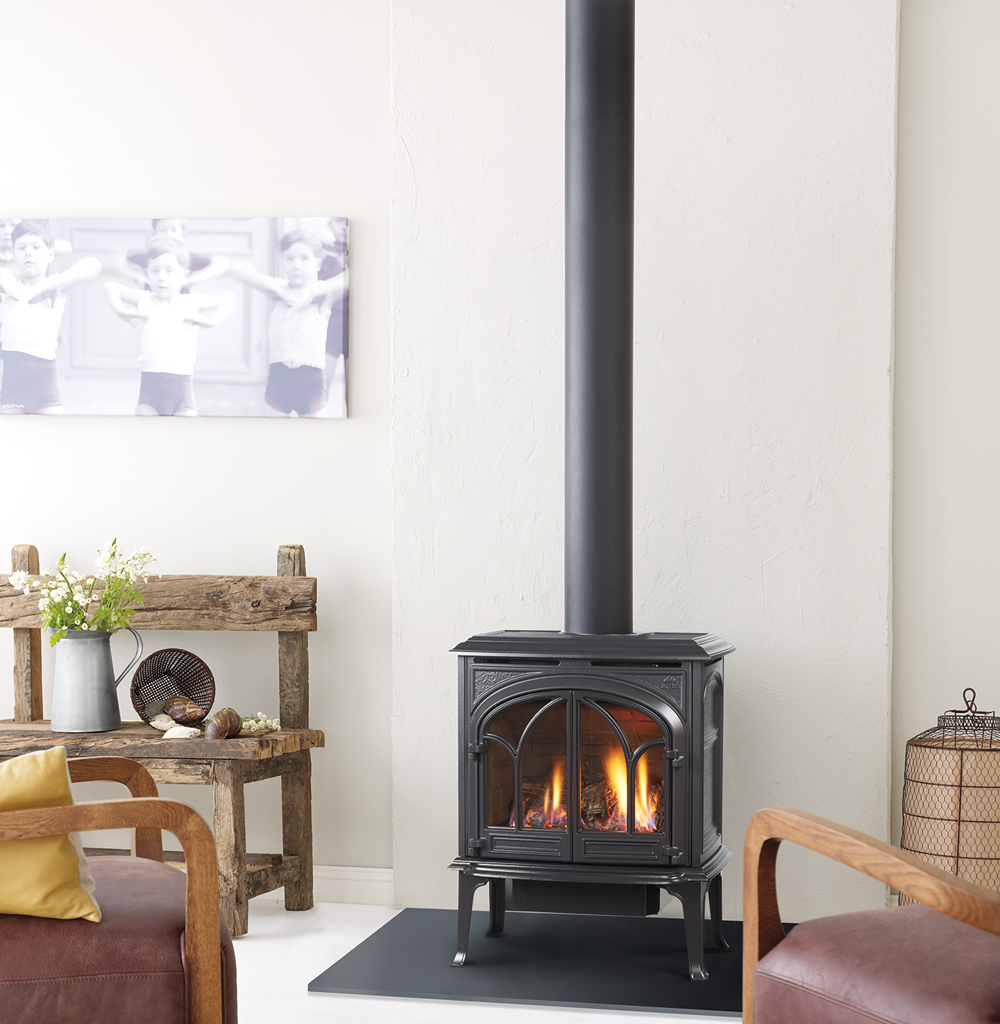 A black gas fireplace with a lit fire, set in a cozy living room with rustic furniture and a black chimney.
