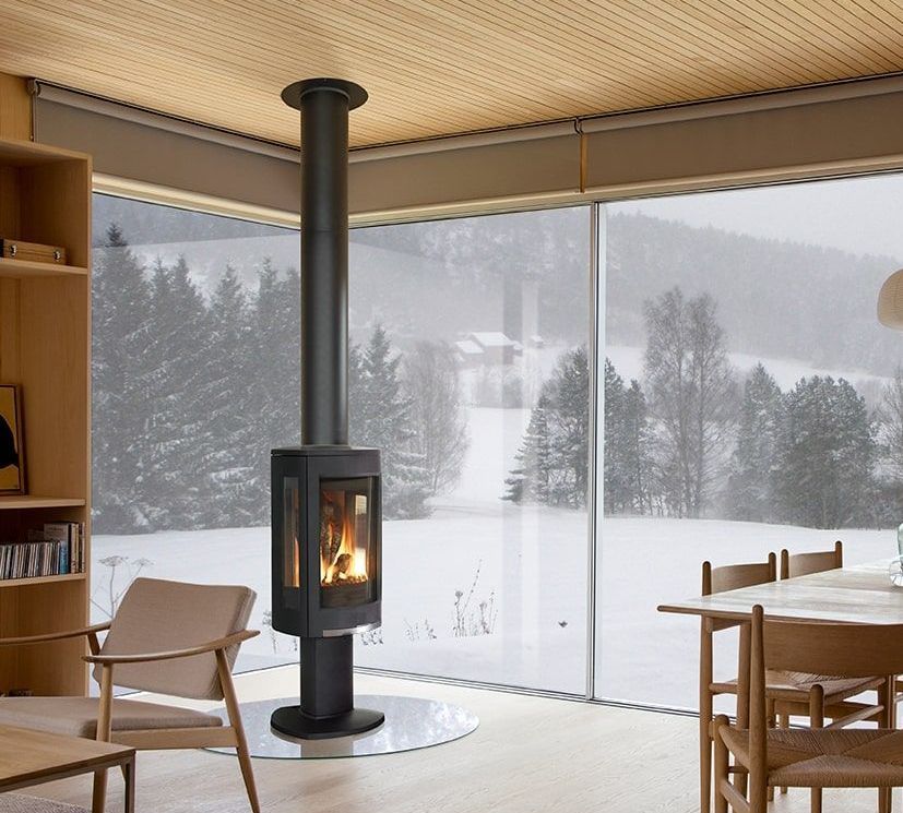 Modern black fireplace with a tall chimney, set in a room with a snowy mountain view through large windows.