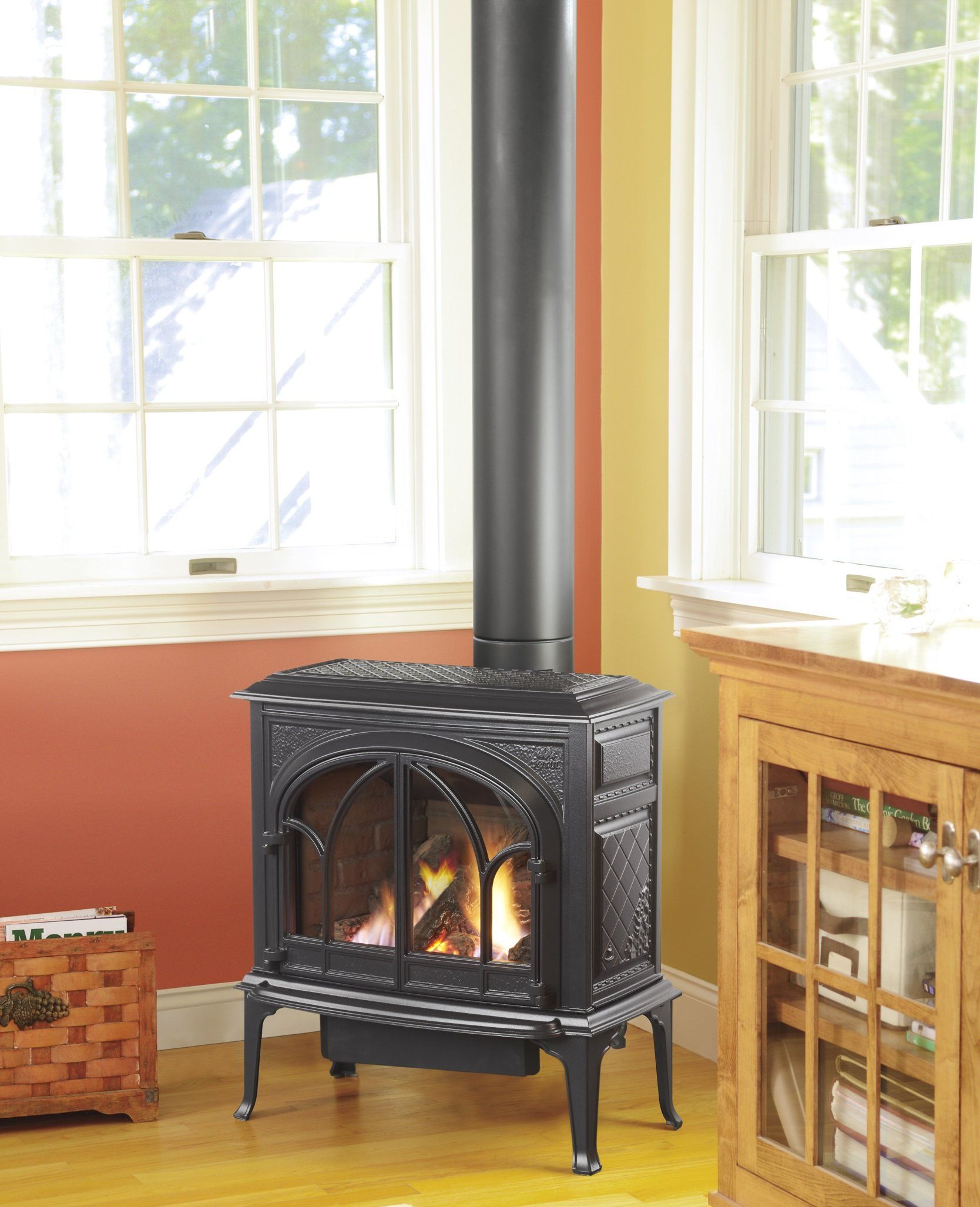 A black gas stove with a lit fire in a room with wooden floors and windows. The walls are red and yellow.