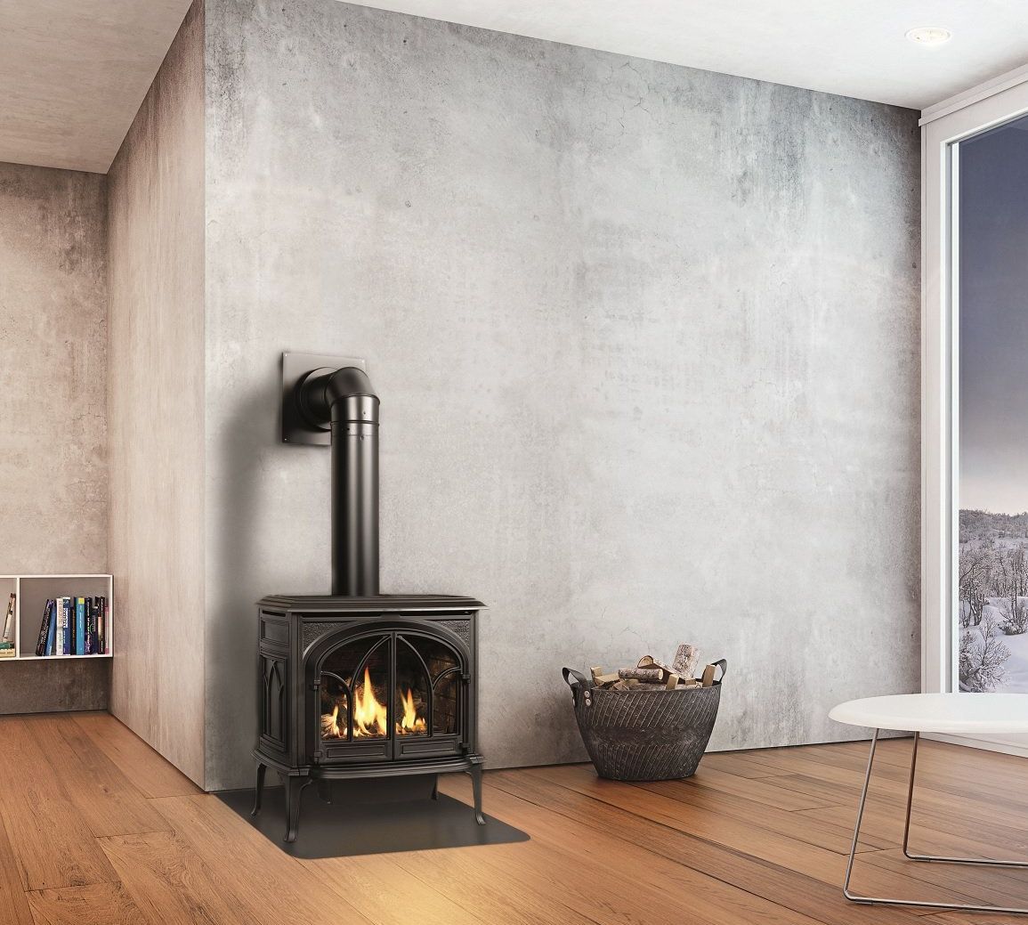 A black cast-iron fireplace with a lit flame sits against a gray concrete wall. Firewood is in a basket nearby.