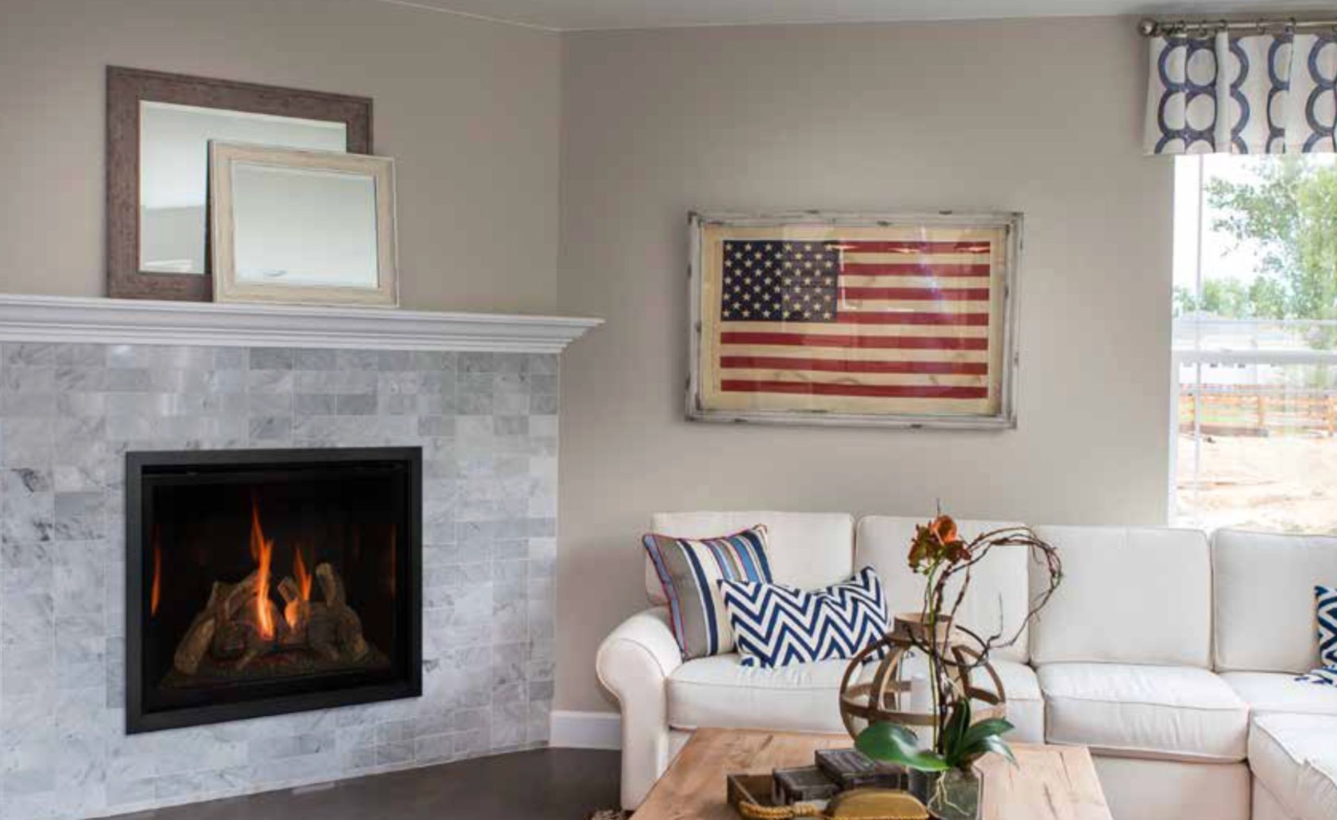 A cozy living room with a fireplace and a white sectional sofa. An American flag painting hangs on the wall.