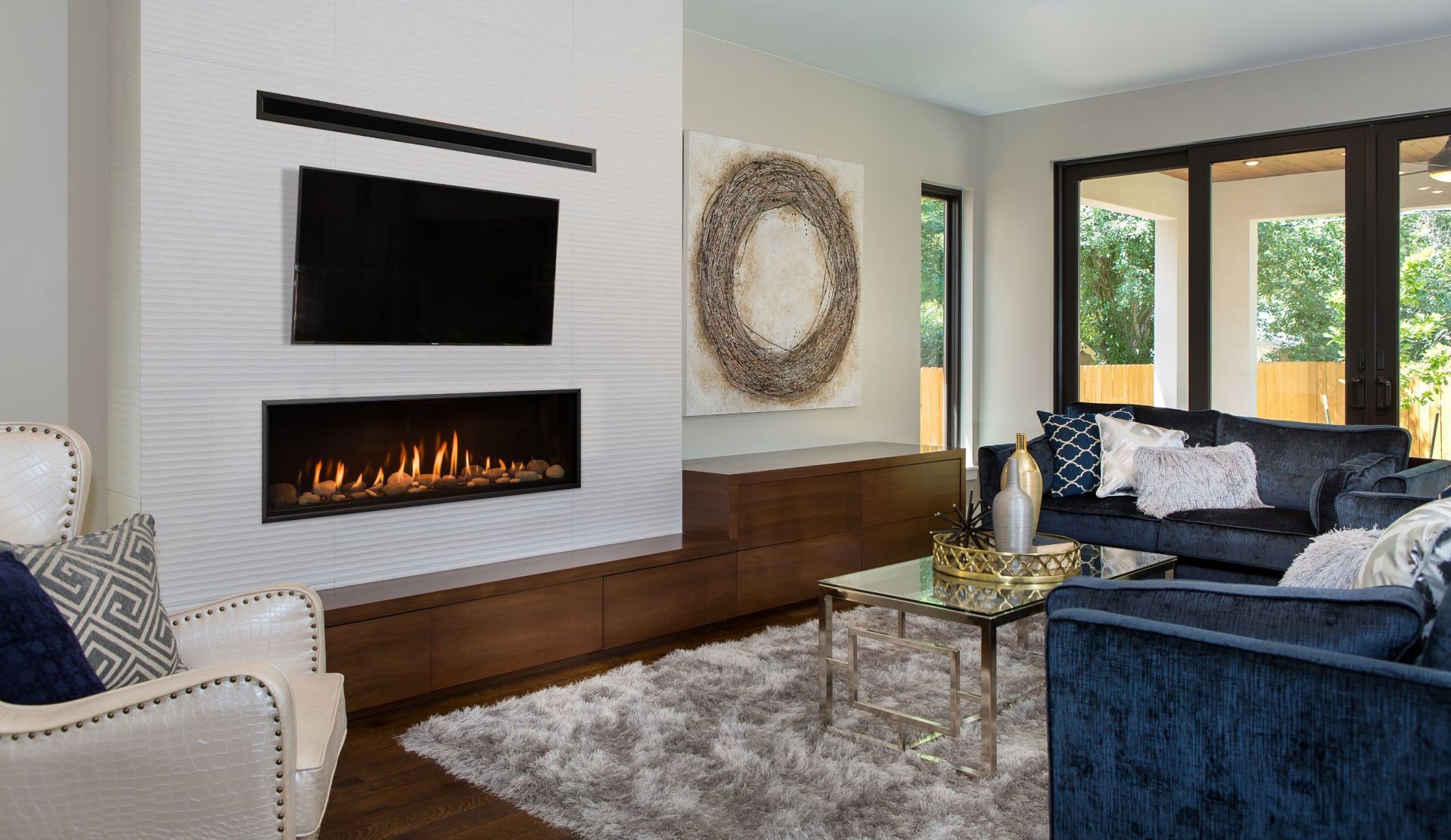 Modern living room with fireplace, TV, and seating. Features a gray rug, marble wall, and dark blue furniture.