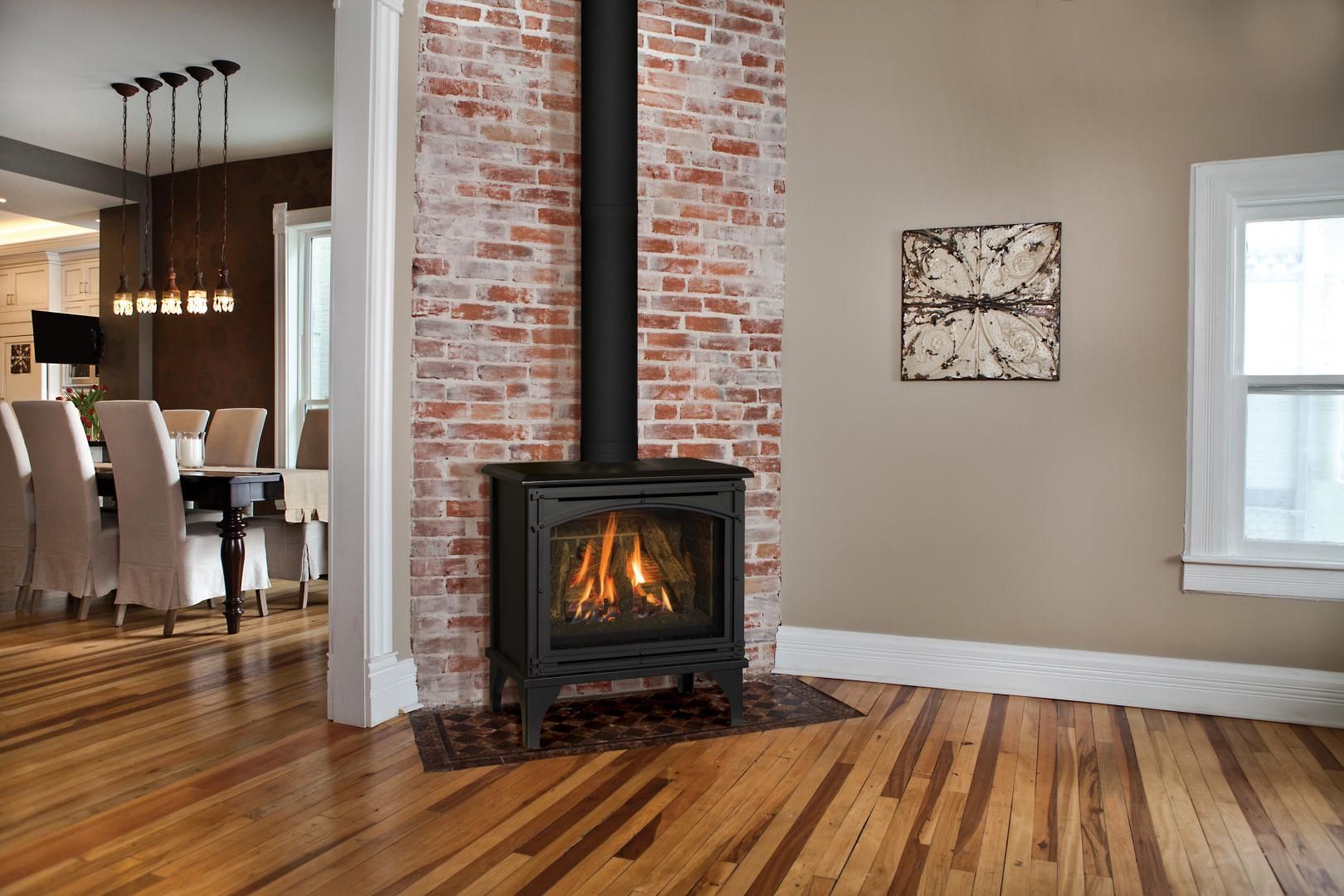 A black fireplace with a brick chimney in a room with hardwood floors. The adjacent room features a dining table.