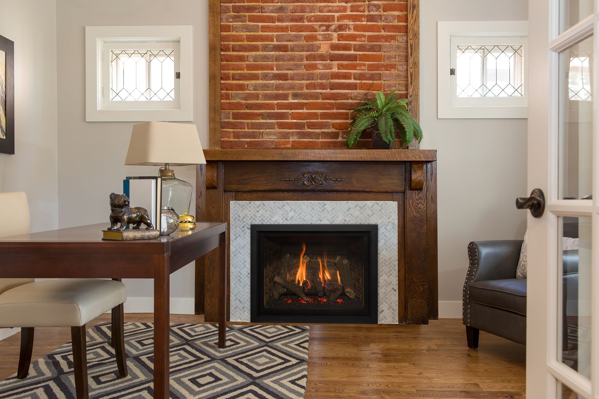 A cozy home office featuring a fireplace with a brick surround, flanked by windows, and a desk.