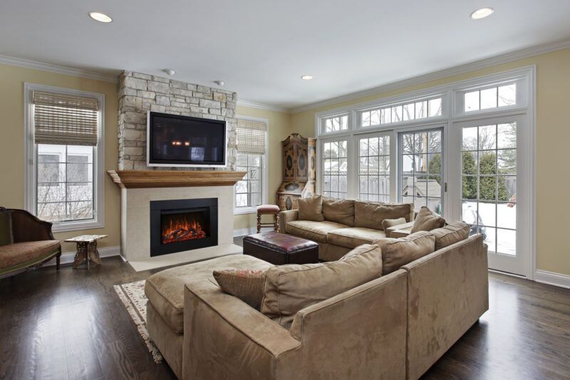 Cozy living room with a fireplace, sectional sofa, and large windows overlooking a snowy outdoor scene.
