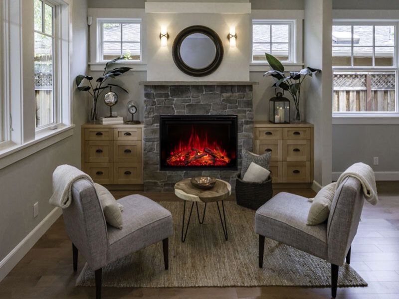 Cozy living room with fireplace, two armchairs facing it, wooden cabinets, round mirror, and small table.