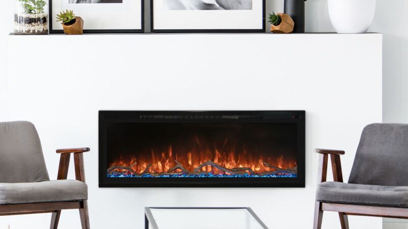 Electric fireplace in a white-walled living room with chairs on either side, simulating flames. Two framed pictures and decor above.