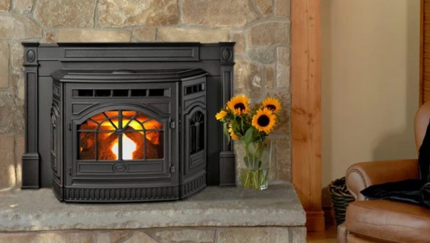 Black pellet stove burning in a stone fireplace. A vase of sunflowers sits nearby, with a leather armchair to the right.