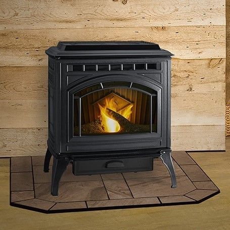 A black pellet stove with a burning flame in front of wood paneling, sitting on a tiled hearth.