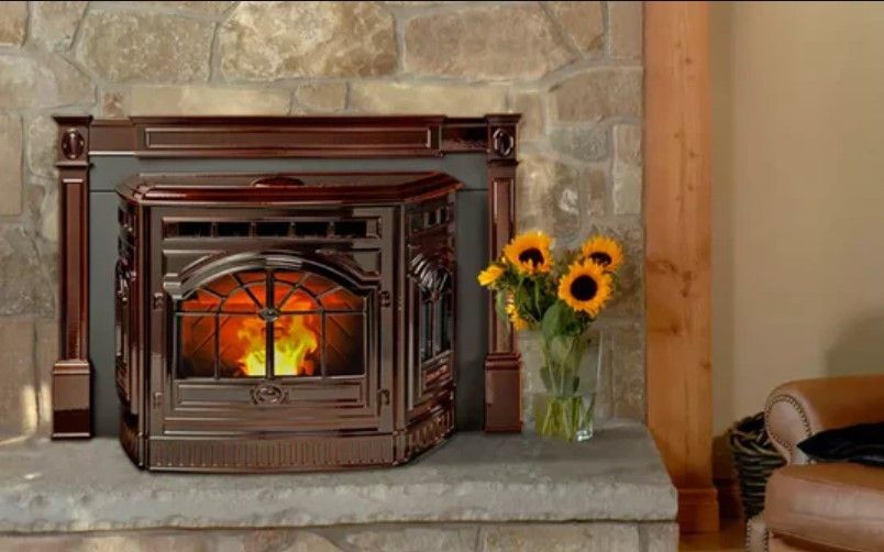 A pellet stove burns brightly in a dark brown hearth, with sunflowers in a vase on the stone hearth. A stone wall forms the backdrop.
