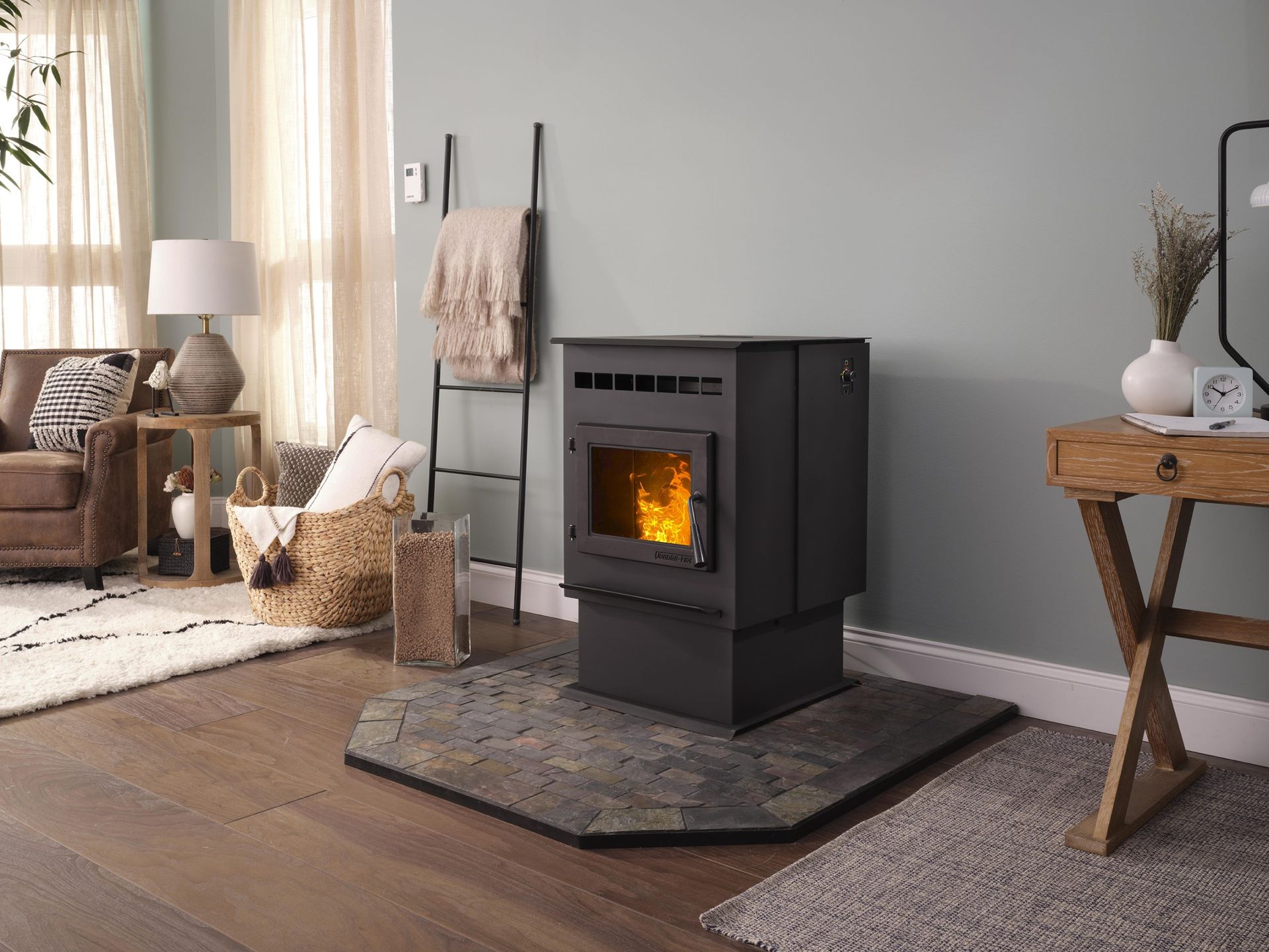 A modern black pellet stove with a lit fire in a living room, set on a slate hearth.