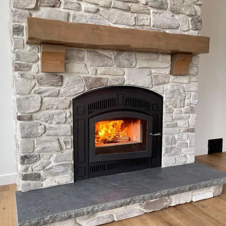 Stone fireplace with burning fire and wooden mantle, with a black insert.