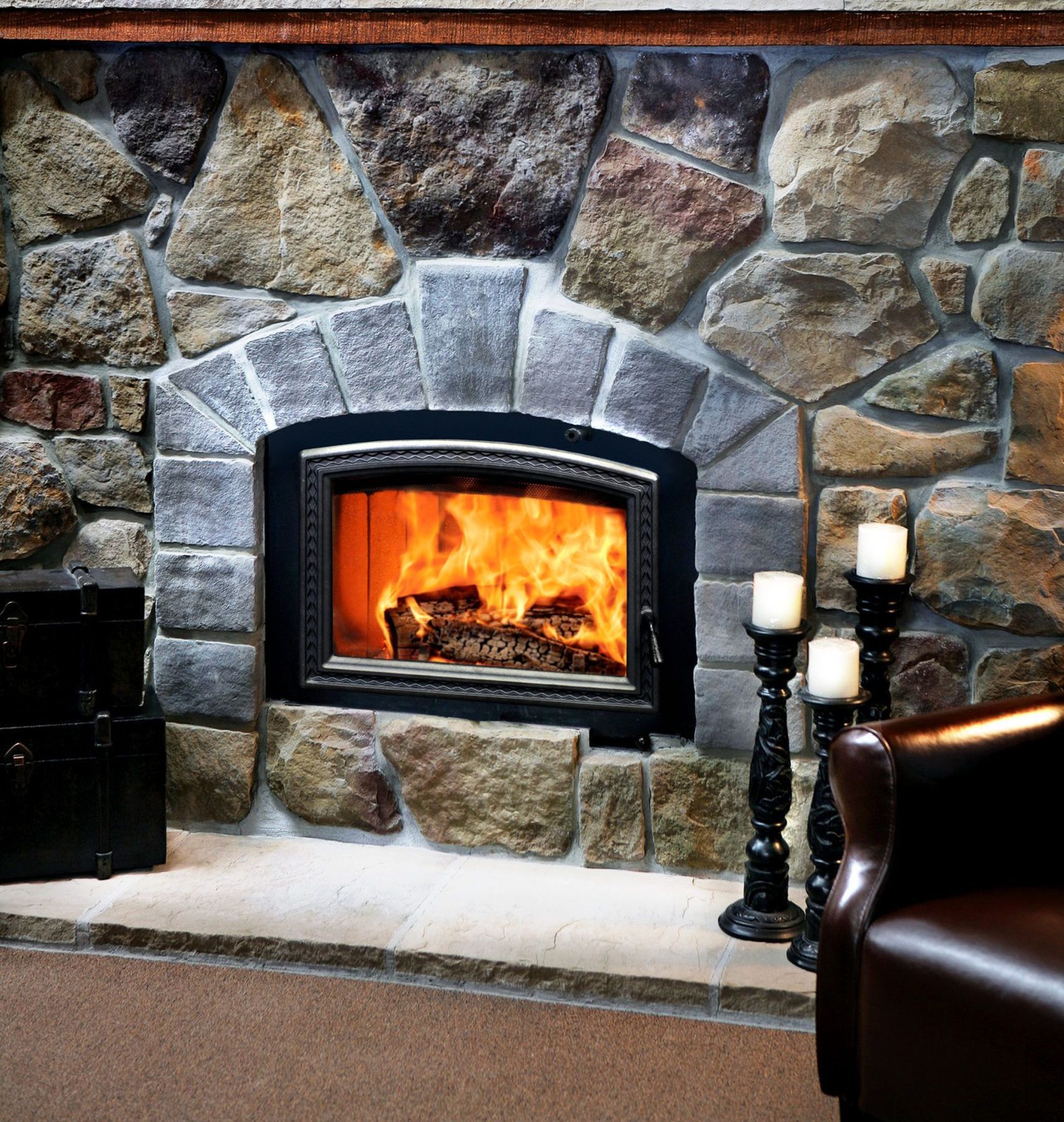 Fireplace with a burning fire, surrounded by stone.  Candles on stands to the right, and a leather armchair is visible.