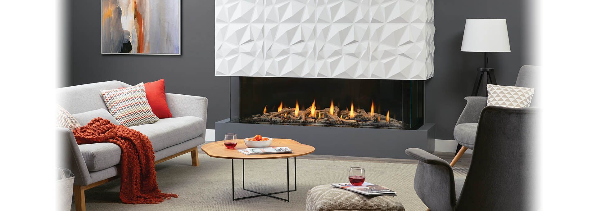 A modern living room featuring a gray couch with orange and patterned pillows, a cozy orange throw, a fireplace with flames, and gray chairs.