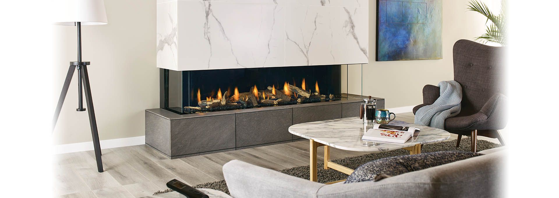 A modern living room featuring a large fireplace with a marble surround. A gray sofa and armchair are arranged around a marble coffee table.
