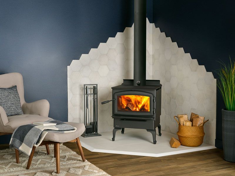 A cozy living room with a black wood-burning stove in a tiled alcove. Fire is visible inside the stove.