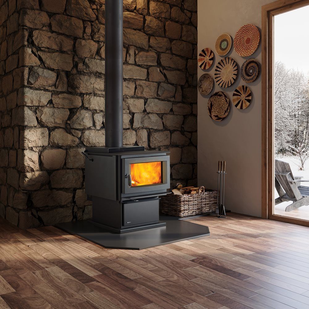 A black wood-burning stove with a lit fire, set against a stone wall in a room with a snowy outdoor view.
