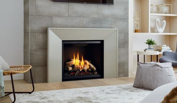 Fireplace with flames, framed in cream-colored border against grey tiled wall.  A living room with neutral colors, and wooden floor.