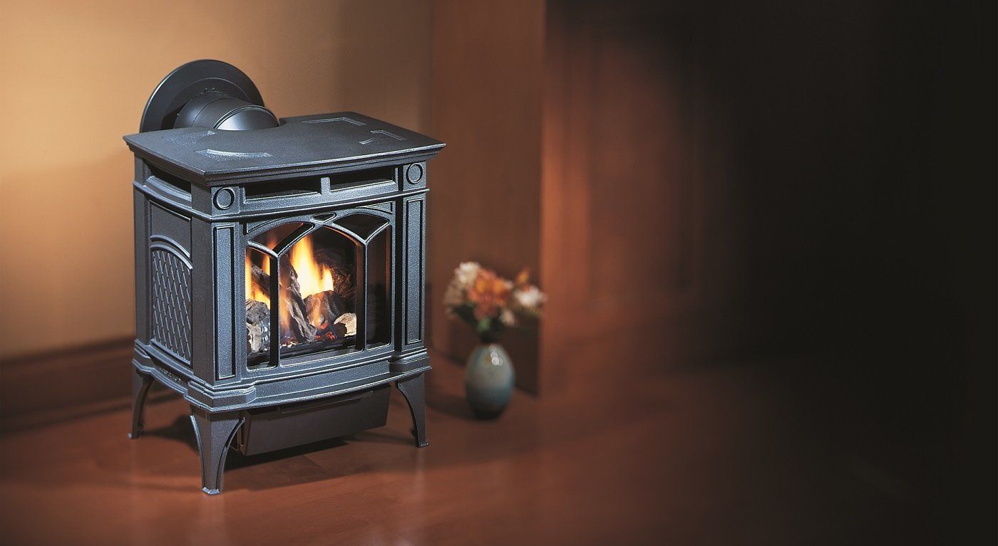 A decorative black gas stove with visible flames, set against a brown wall and floor. A vase of flowers sits nearby.