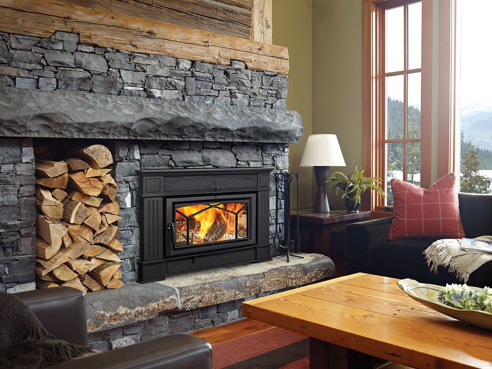 Fireplace in a rustic living room. A stone fireplace with burning fire and wood storage, brown leather chairs, and wooden table.