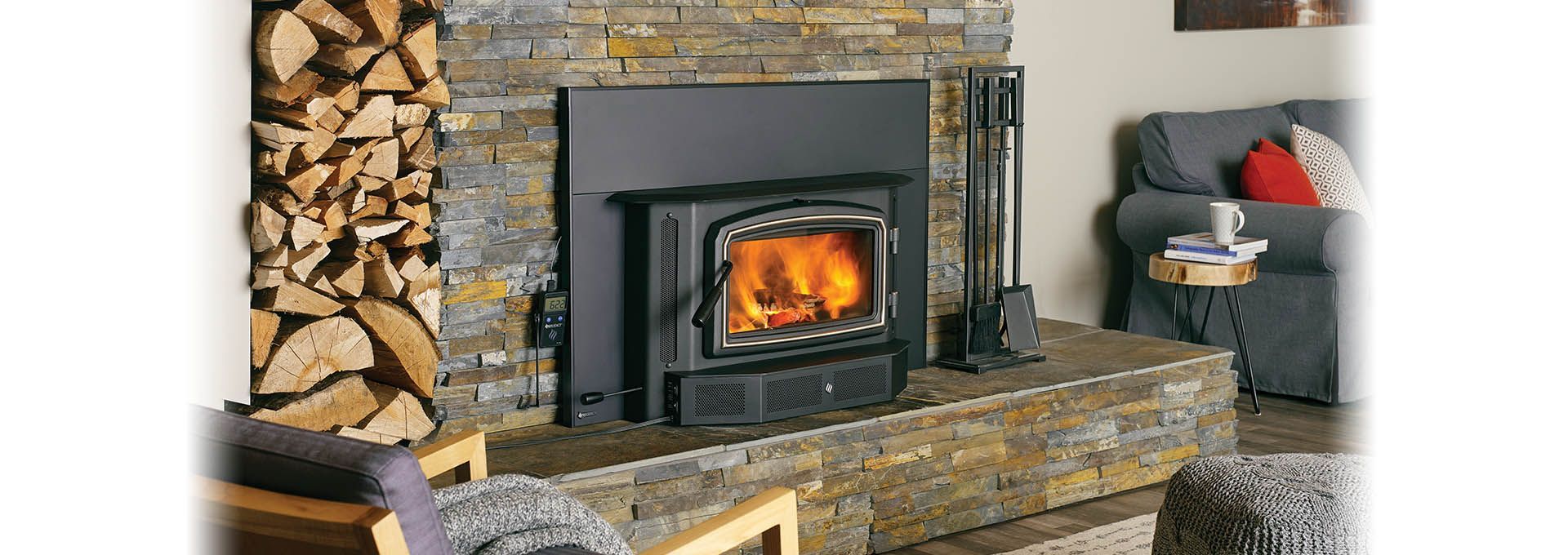 A fireplace with a lit fire, stacked wood, and a seating area in a cozy living room.