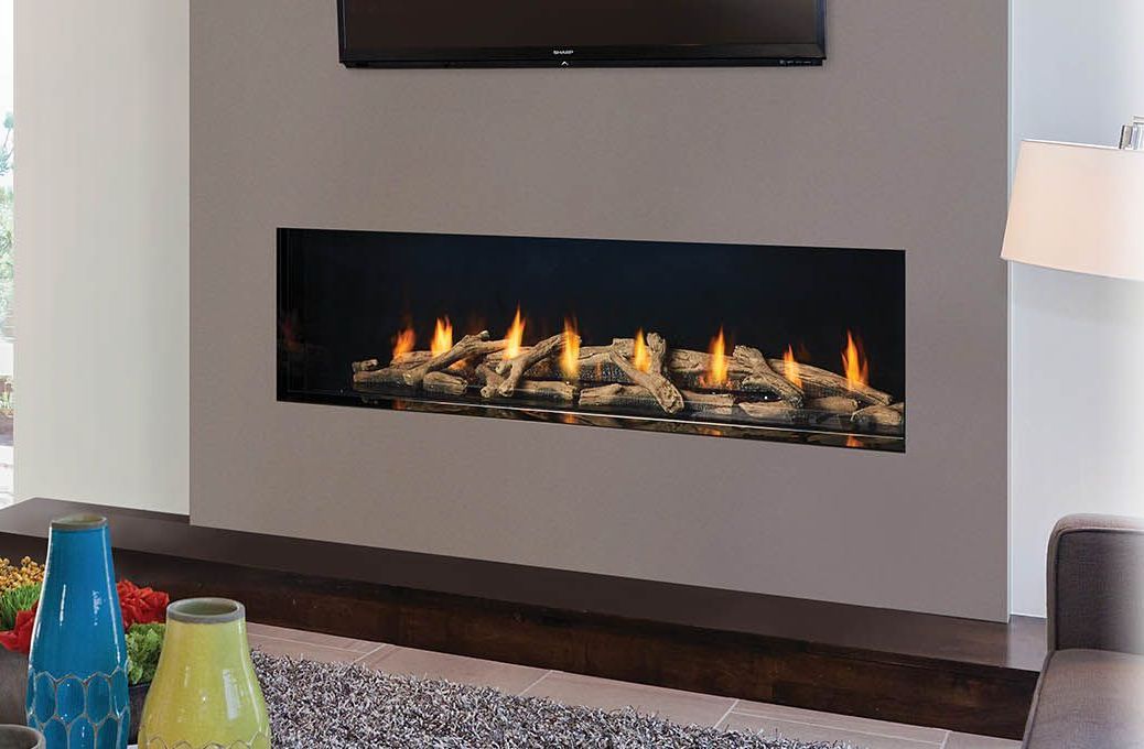 A modern fireplace built into a gray wall with a TV above, logs and flames visible.