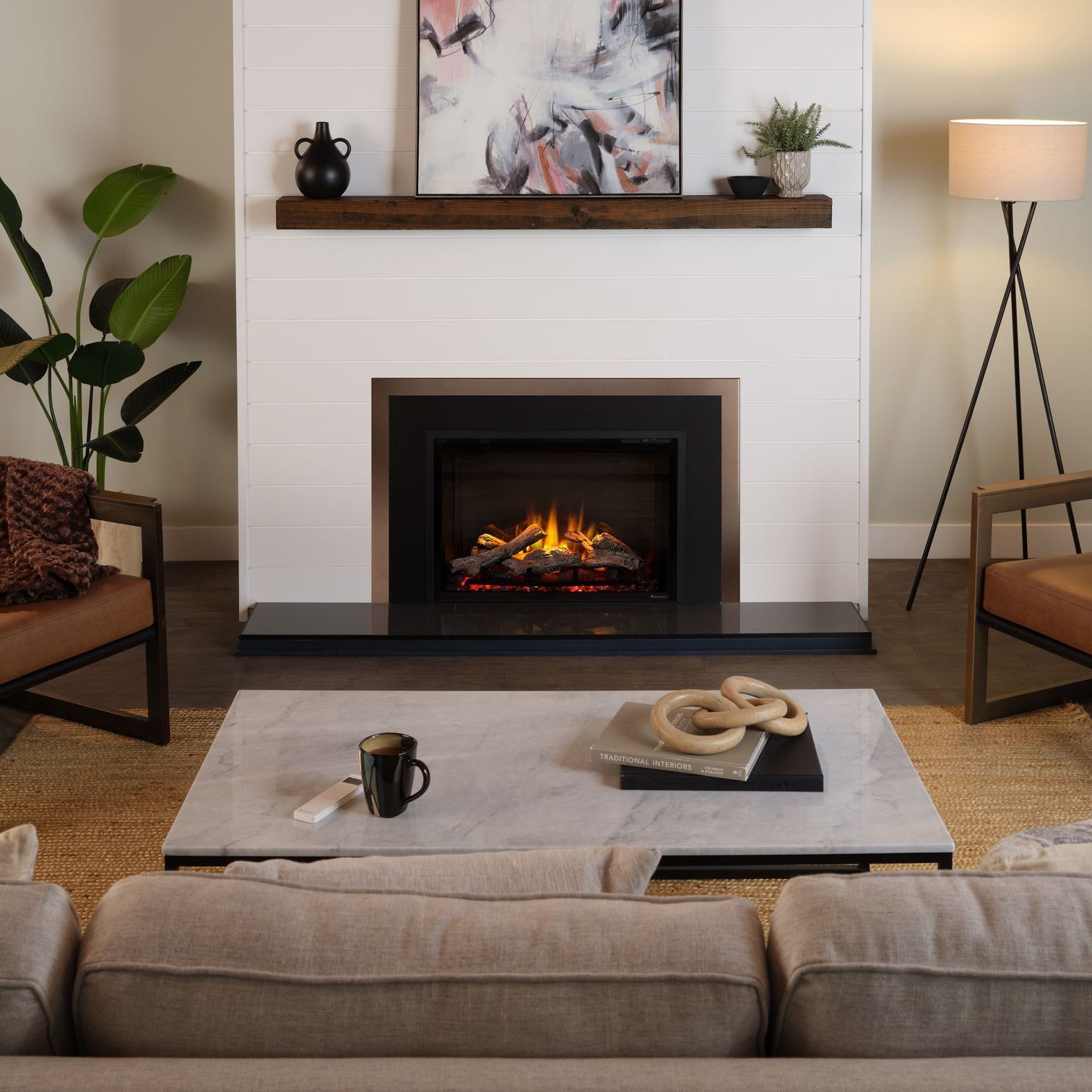 Living room with fireplace, modern furniture, and decorative items. Neutral tones dominate, featuring a white wall, dark hearth, and a lit fireplace.