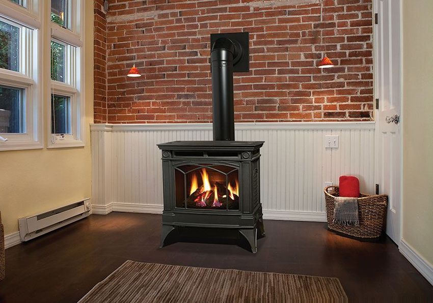 A lit gas fireplace with a black chimney against a red brick wall and white wainscoting in a cozy room.
