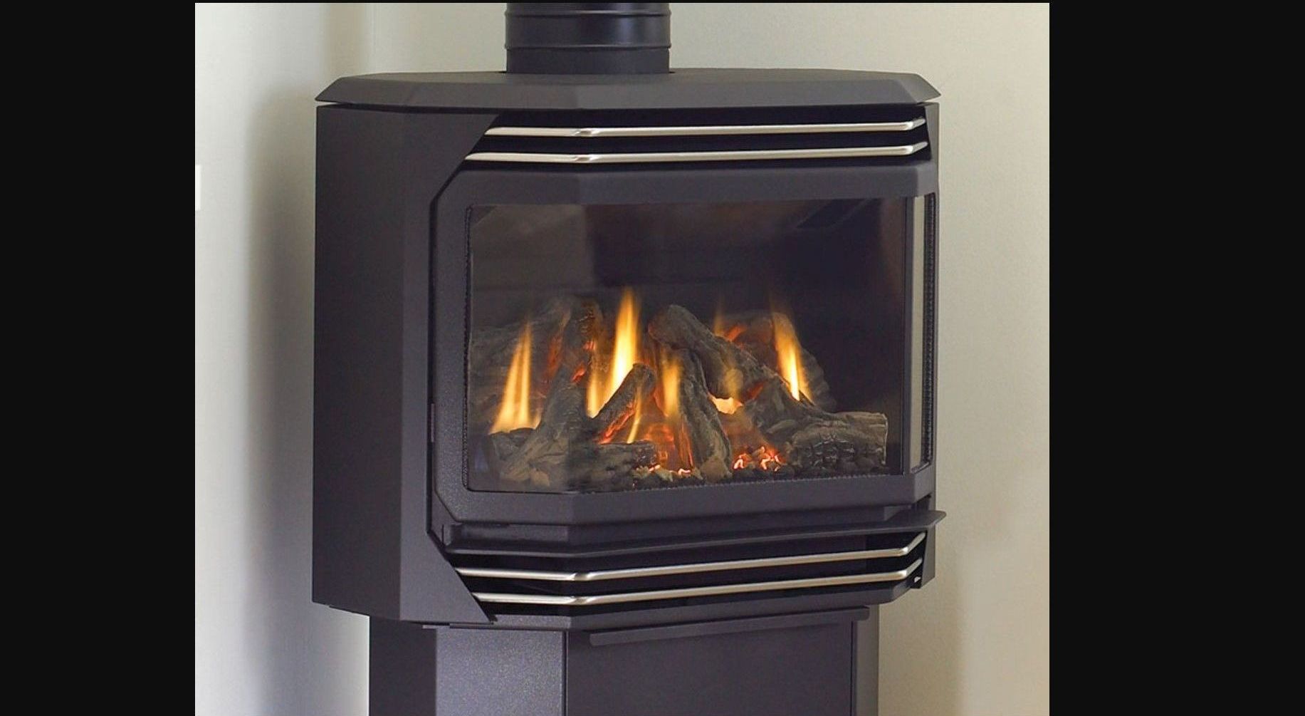 A black gas fireplace with a glass front showing burning flames and artificial logs. It is installed against a white wall.