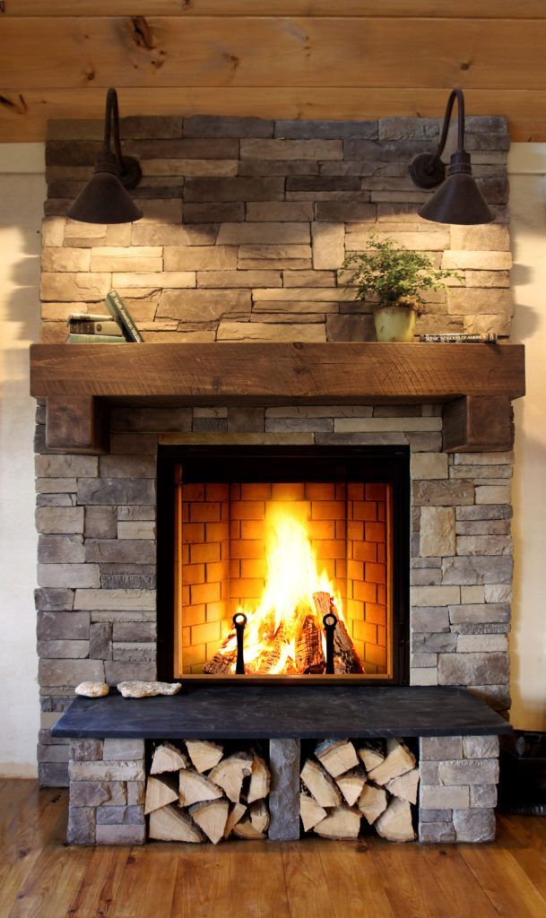Fireplace with stone surround, wooden mantel, and built-in wood storage, flames burning brightly.